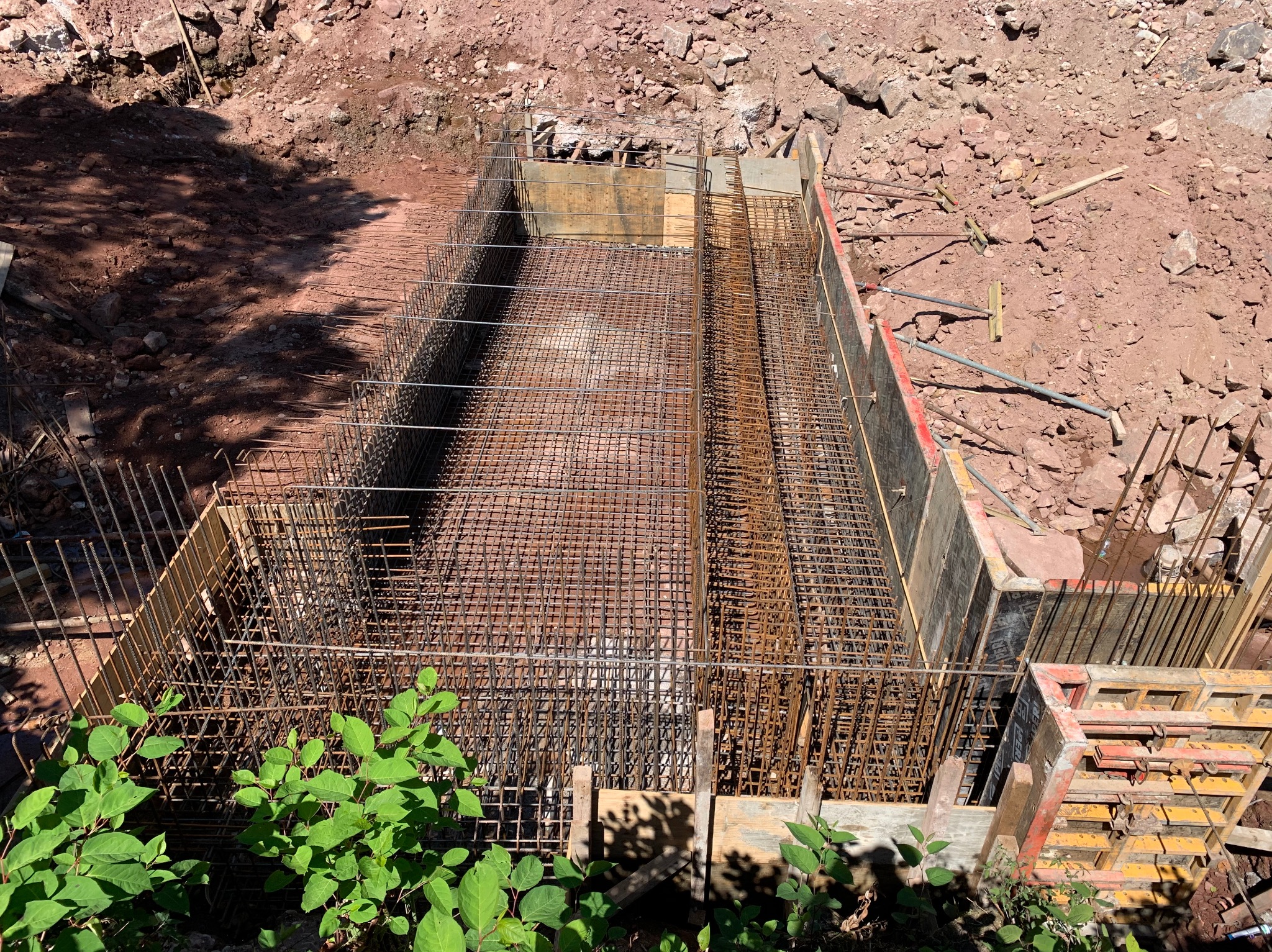Zbrojenie w szalunku, widok z góry. Stalowa siatka w drewnianej formie, przygotowana do zalania betonem. Ziemne tło, roślinność w dolnej części kadru.