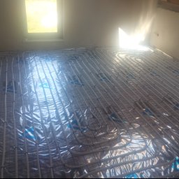 HYDROMAR - Ułożone rury ogrzewania podłogowego na folii izolacyjnej w jasnym pomieszczeniu z oknem. Widok z góry ukazuje regularny wzór instalacji.