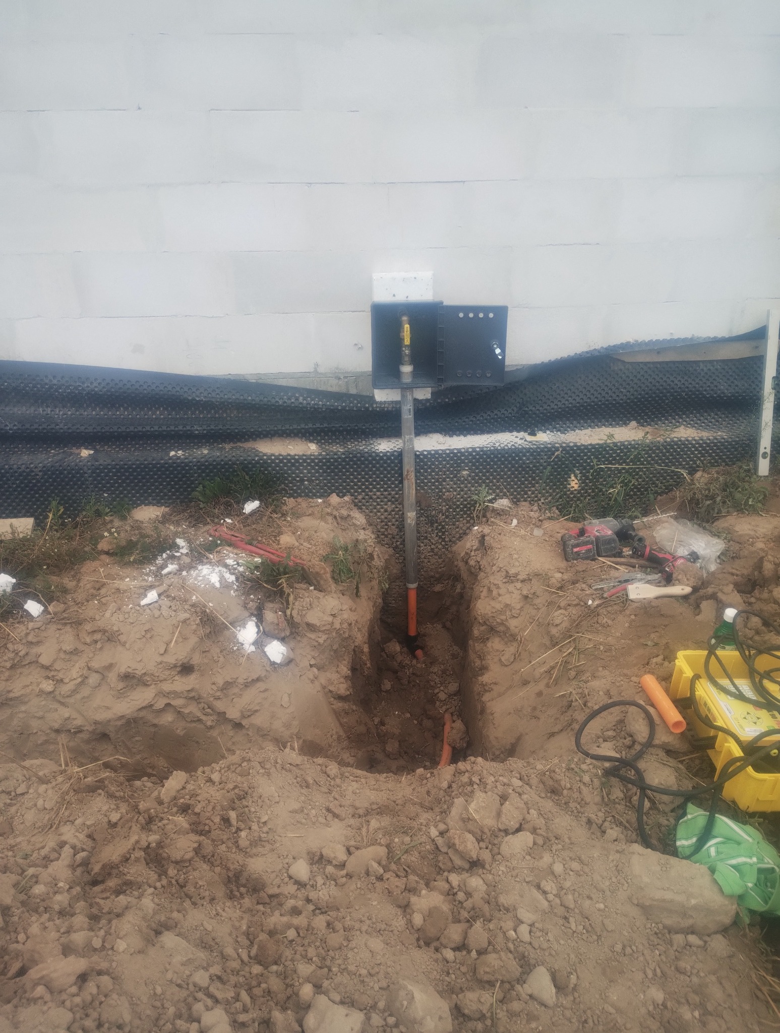 Przyłącze gazowe w wykopie, widoczna skrzynka przyłączeniowa na ścianie budynku, narzędzia pracy obok. Etap prac ziemnych i montażu instalacji.