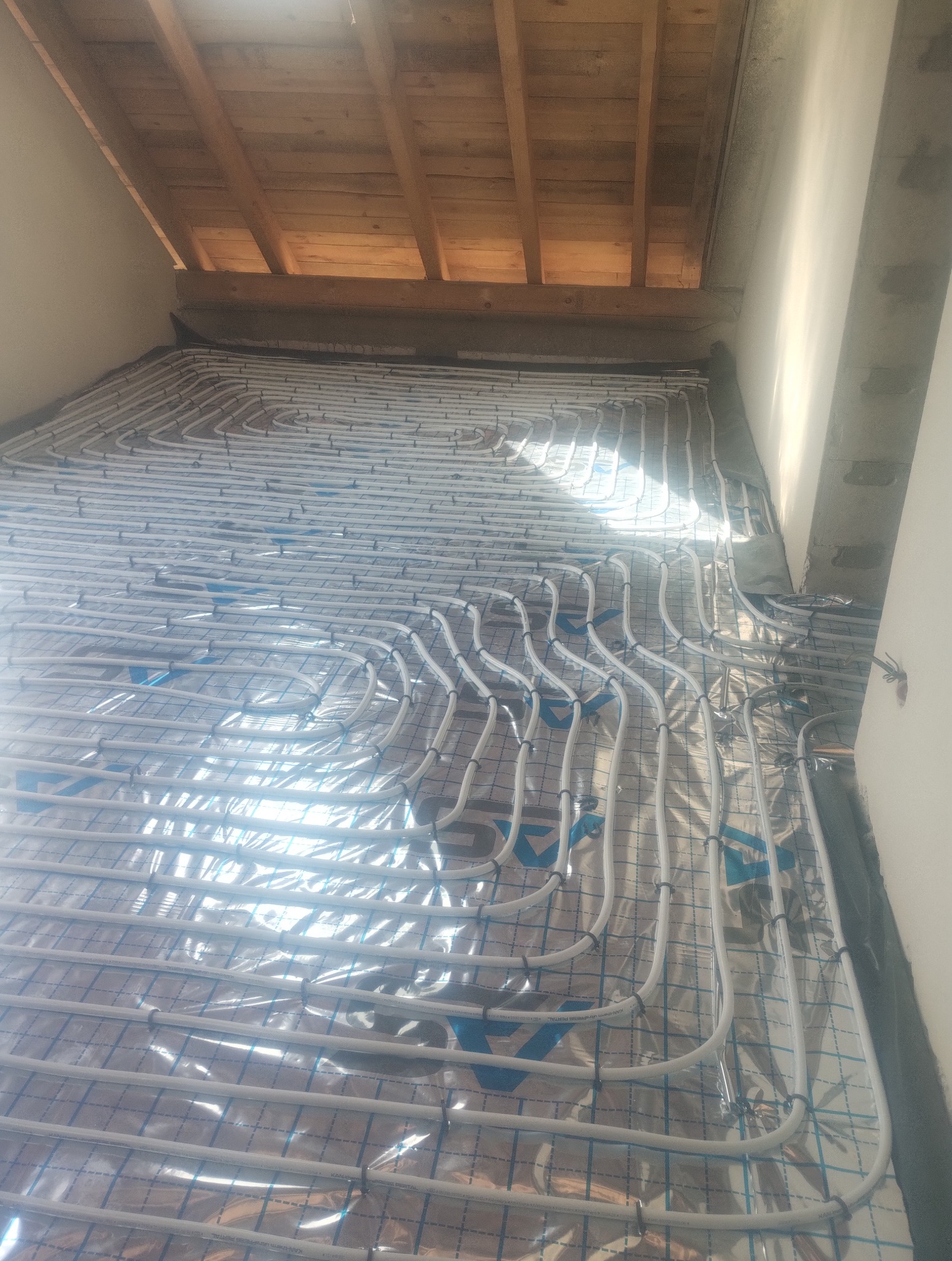 Ułożone rury ogrzewania podłogowego na folii aluminiowej w nowym budynku, widok z góry, surowy stan wykończenia, drewniany strop.