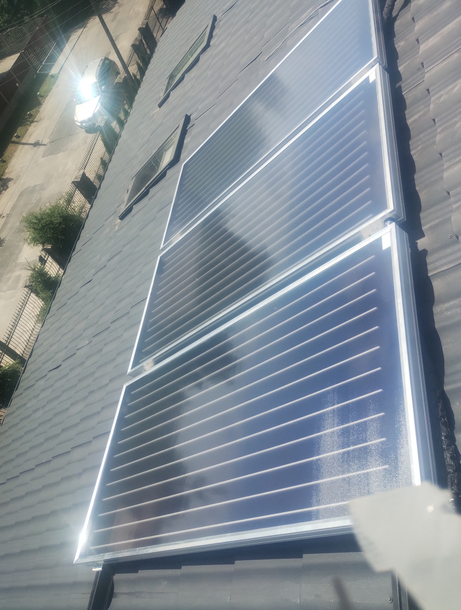 Zamontowane panele słoneczne na dachu pokrytym gontem bitumicznym. Widok z góry, jasne odbicie słońca. Ujęcie w lekkim skosie.