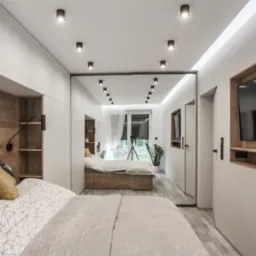 Nowoczesna sypialnia z lustrzaną ścianą, wbudowaną szafą i telewizorem. Drewniane akcenty, designerskie lampki nocne i minimalistyczny wystrój tworzą przytulną atmosferę.