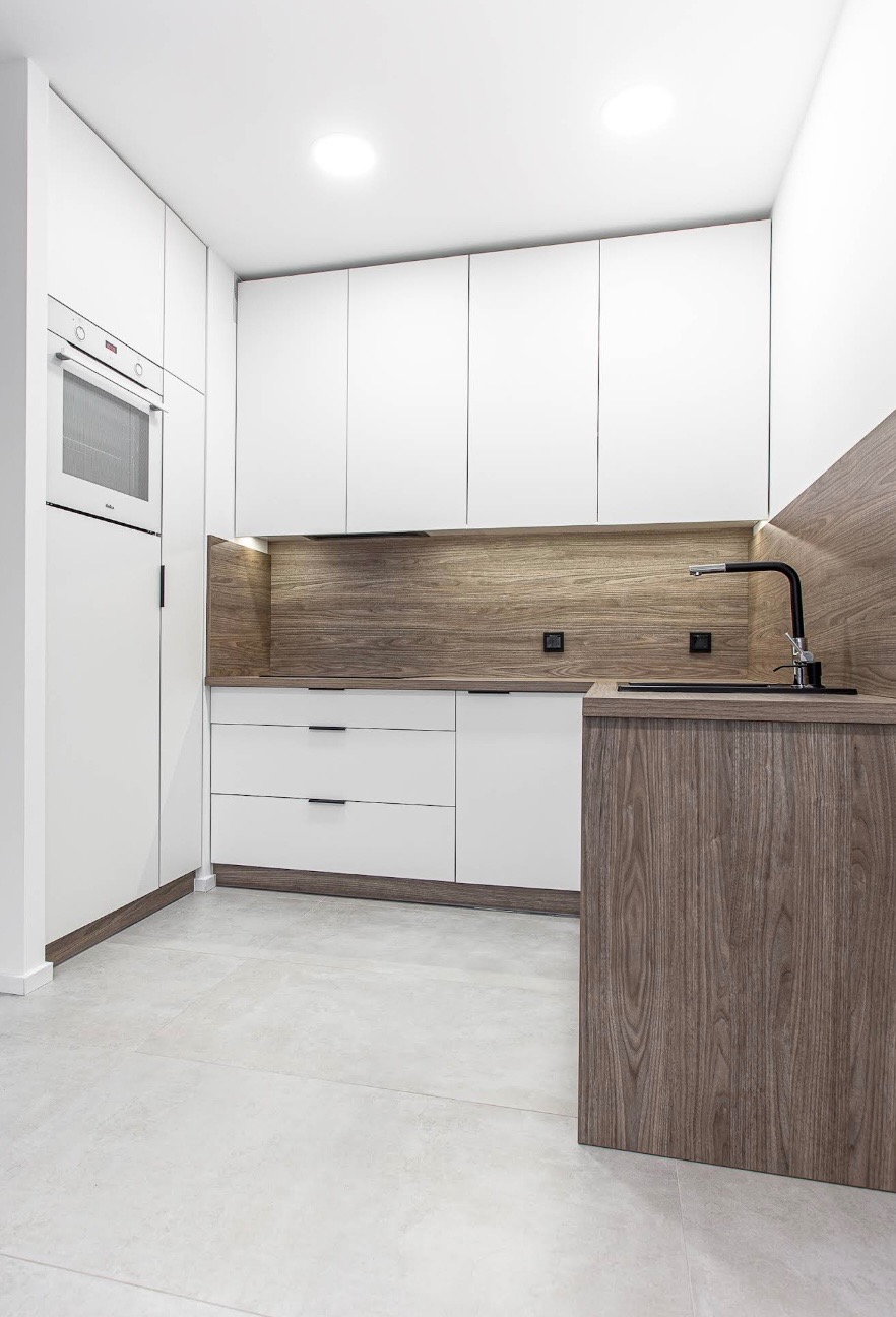 Nowoczesna kuchnia w Katowicach: białe fronty szafek, drewniany blat i panel ścienny, czarna armatura. Minimalistyczny design, oświetlenie LED.