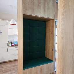 YO Meble - Wnęka z siedziskiem i zielonym obiciem, wbudowana w drewnianą zabudowę kuchenną z szafkami. Widok na białą kuchnię i podłogę z paneli.