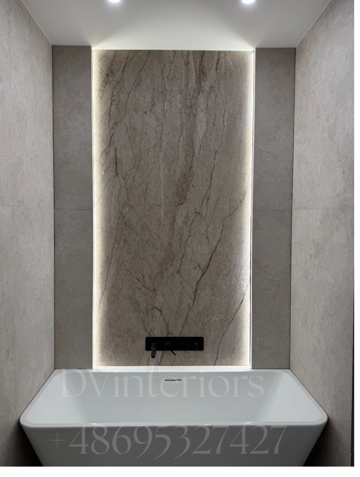 Minimalistyczna łazienka z wanną, podświetloną ścianą z płytek imitujących marmur i czarną armaturą. Jasne płytki na ścianach i suficie.