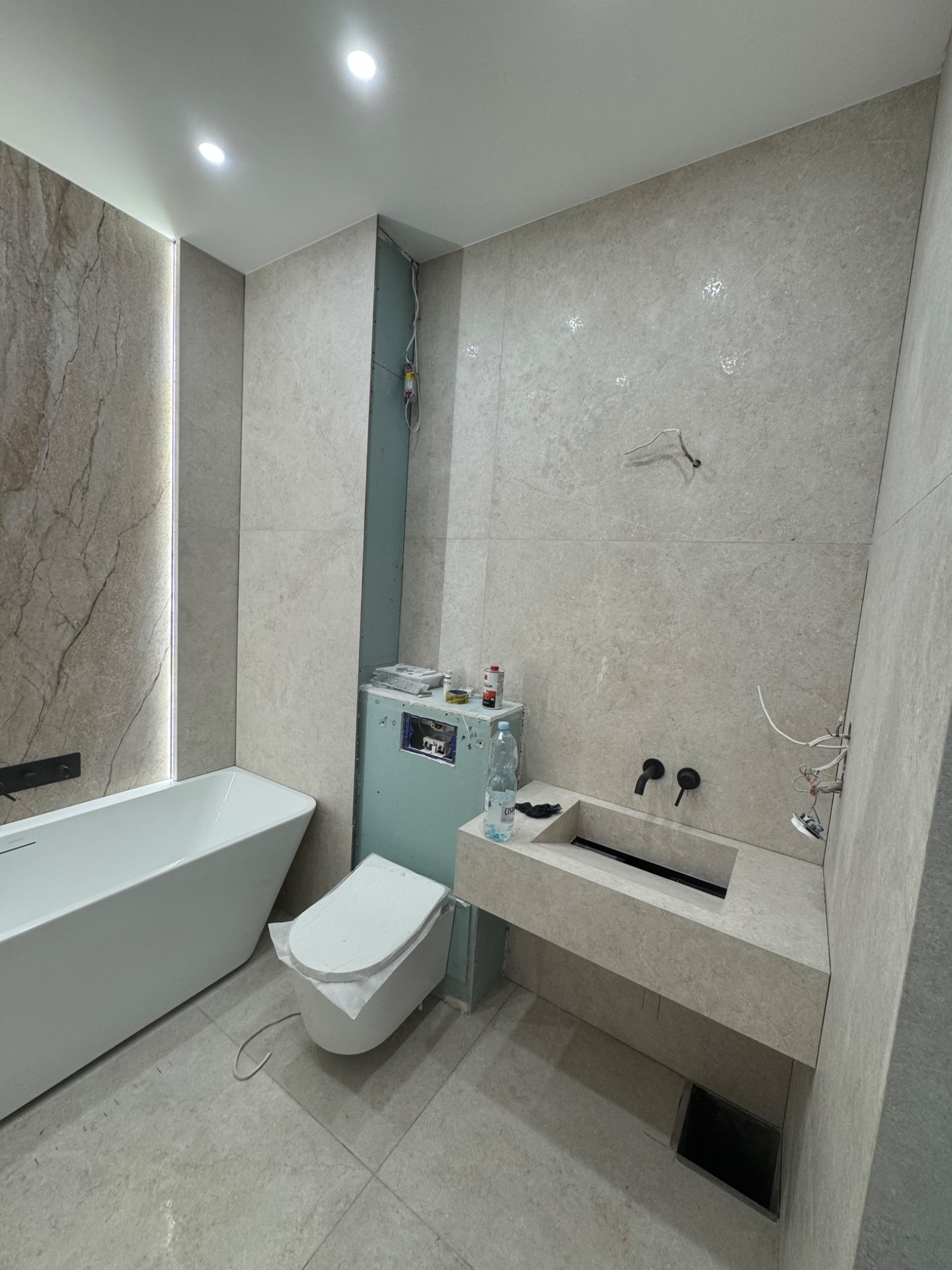 Jasna łazienka w trakcie wykończenia: wanna, toaleta, umywalka z czarną armaturą. Widoczne niedokończone instalacje elektryczne i sanitarne.