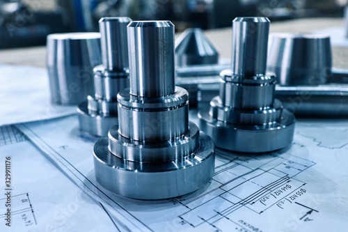 Metalowe elementy na planie technicznym, w chłodnej tonacji. Widoczne detale obróbki i precyzja wykonania. Elementy ułożone na rysunku technicznym.