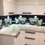 Białe szafki kuchenne z czarnym panelem szklanym z motywem kwiatowym, widoczne podświetlenie blatu i czarne uchwyty szafek.