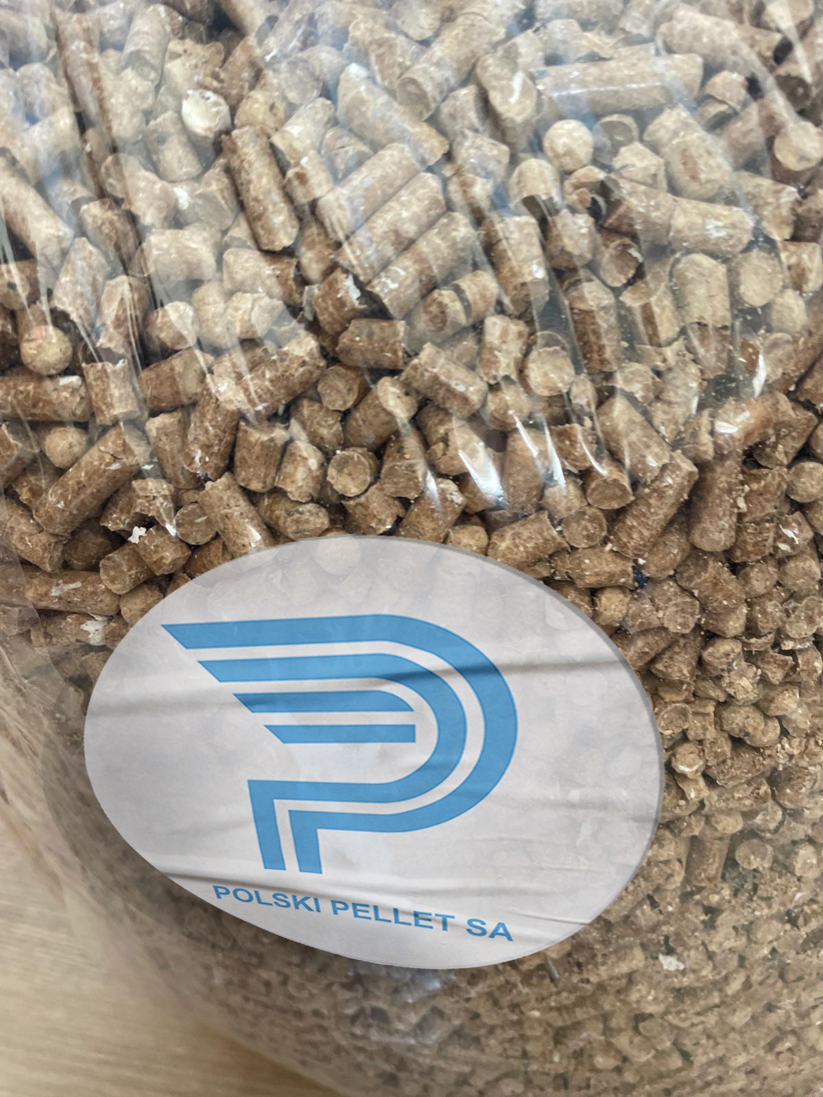 Jasnobrązowy pellet drzewny w przezroczystym worku z niebieskim logo 'P' i napisem 'POLSKI PELLET SA'.