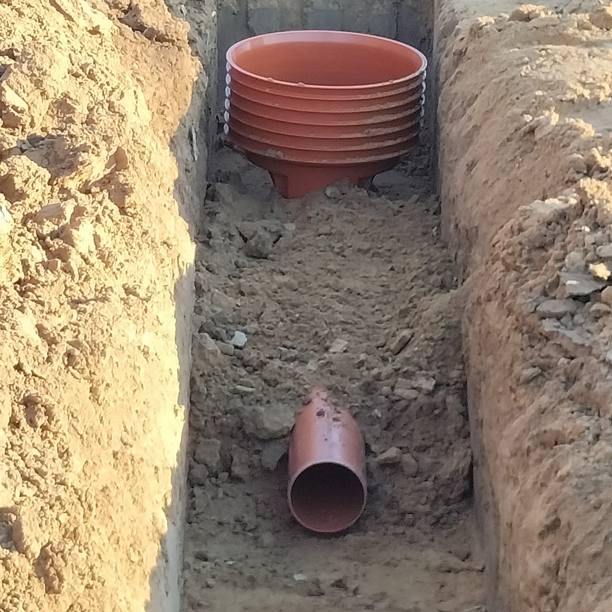 Rów z terakoty: studzienka drenażowa i rura w ziemi. Widok z góry na wykopany rów z elementami instalacji drenażowej.