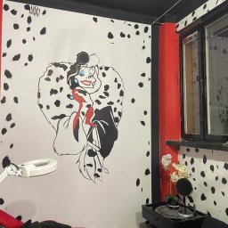 Serhii Burlin - Pokój z motywem Cruelli De Mon: białe ściany w czarne kropki, czerwony akcent przy oknie i duży rysunek postaci. Widoczna lampa powiększająca i dekoracje.