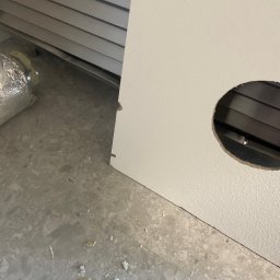 Serhii Burlin - Białe drzwi z wyciętym okrągłym otworem, widoczna kratka wentylacyjna. Na podłodze resztki materiałów budowlanych. W tle kratka wentylacyjna.