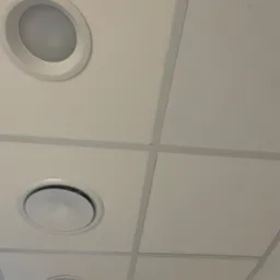 Kasetonowy sufit podwieszany z trzema okrągłymi oprawami oświetleniowymi. Widok z dołu, oświetlenie równomierne, jasne panele.