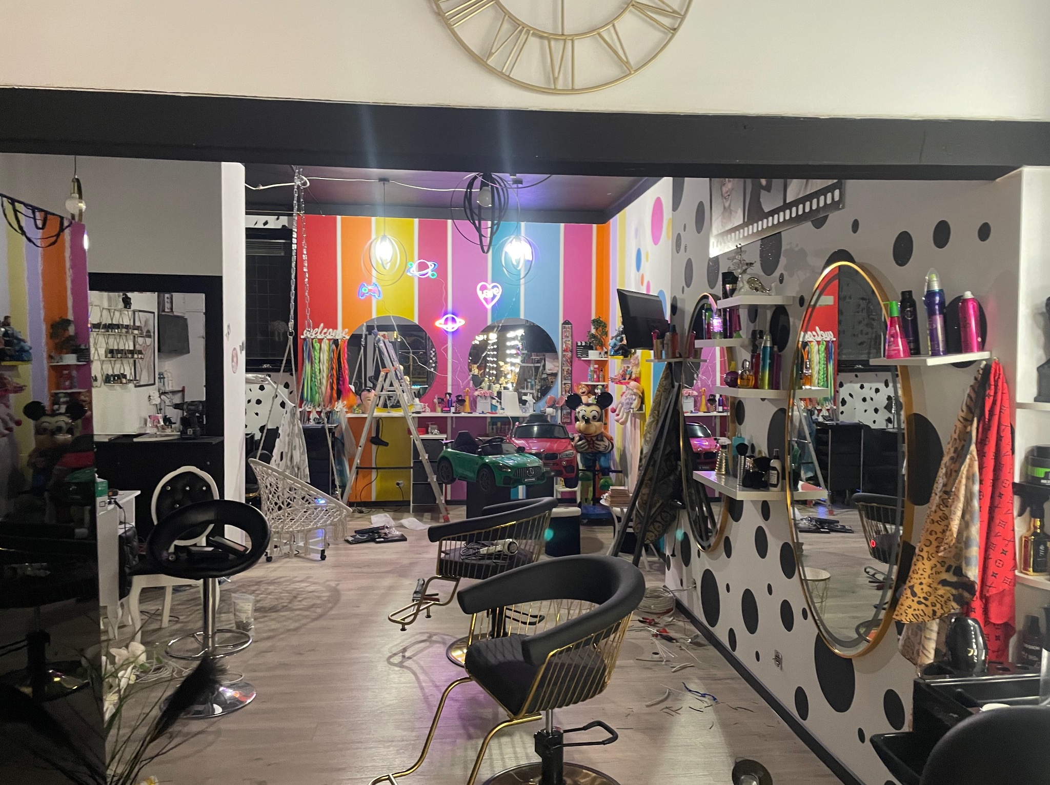 Wnętrze salonu fryzjerskiego z kolorowymi ścianami, lustrami i fotelami. Widoczne narzędzia fryzjerskie i dekoracje, tworzące unikalny, artystyczny wystrój.