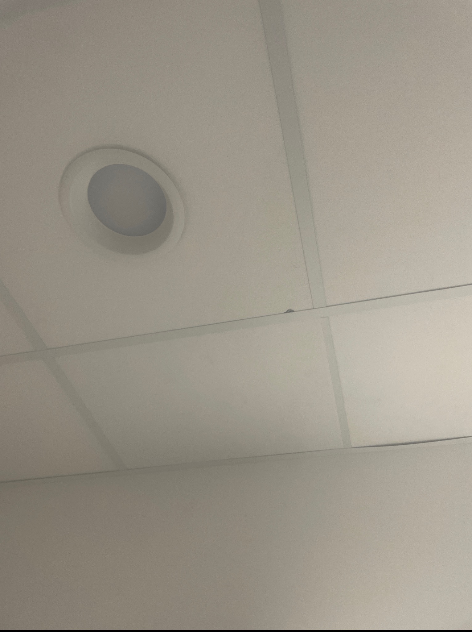 Kasetonowy sufit podwieszany z okrągłym, wpuszczanym oświetleniem LED. Widok z dołu, ukazujący strukturę sufitu i detale oprawy oświetleniowej.