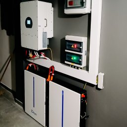 Innowacyjny Dom - Kompletna instalacja magazynu energii Deye z inwerterem i zabezpieczeniami. Widoczne okablowanie i podłączenia. Szara ściana, betonowa podłoga.