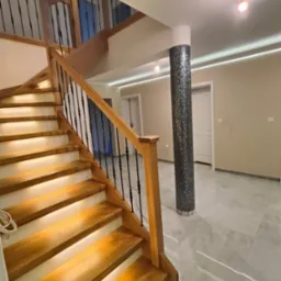 Nowoczesne schody drewniane z podświetleniem LED, czarne balustrady, kolumna wykończona mozaiką w przestronnym holu z marmurową podłogą i oświetleniem sufitowym.