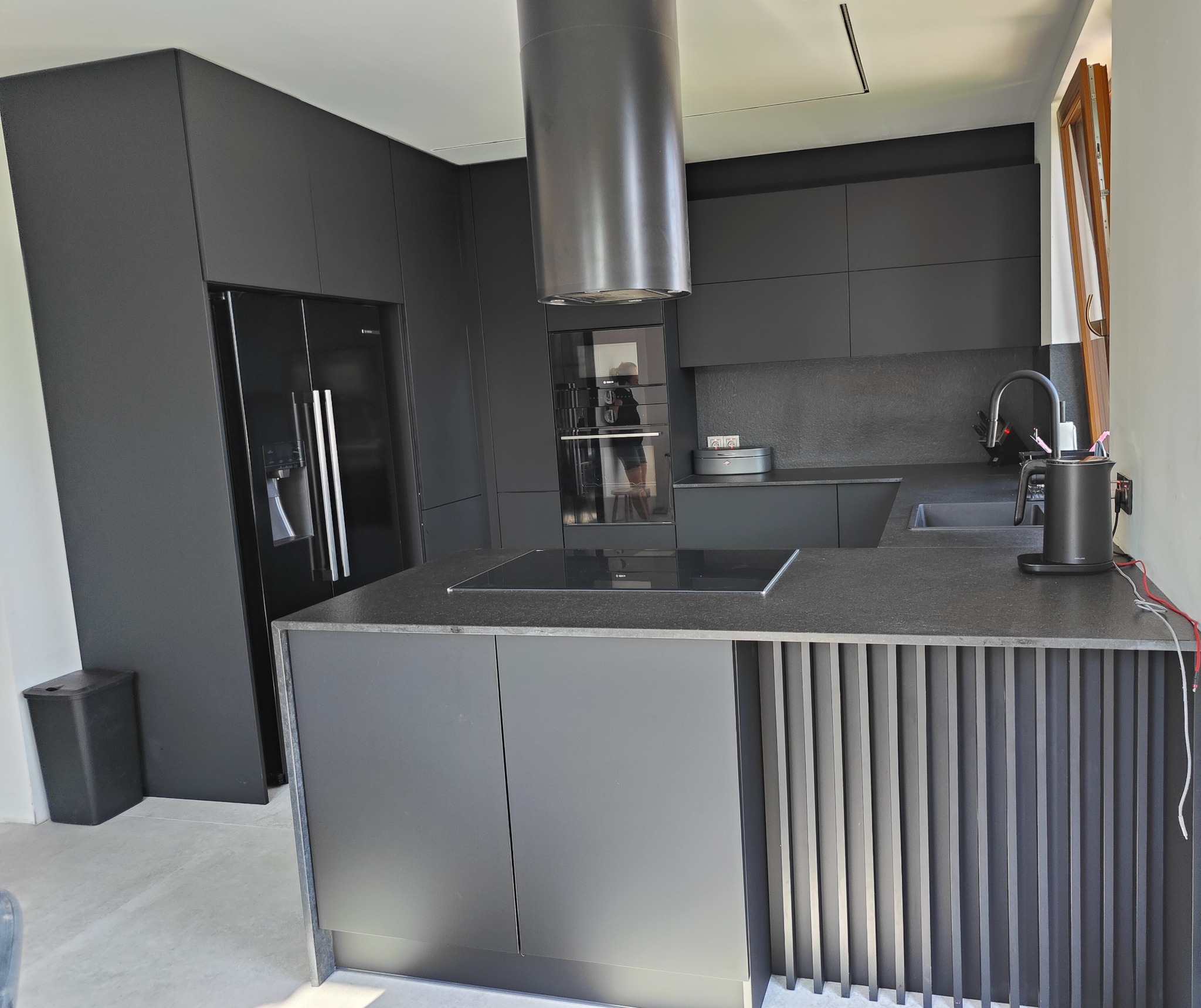 Nowoczesna, grafitowa kuchnia z wyspą i sprzętami marki Bosch. Minimalistyczny design z elementami dekoracyjnymi na wyspie.