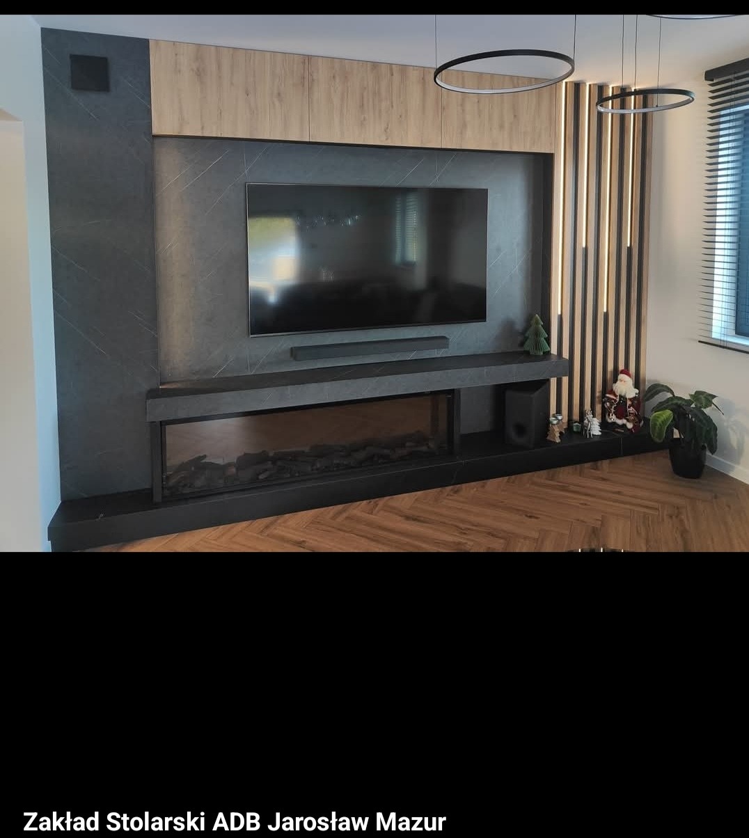 Stylowa zabudowa ściany z telewizorem, imitacją kominka i drewnianymi lamelami. Podwieszane, okrągłe lampy. Dekoracje świąteczne i parkiet w jodełkę.