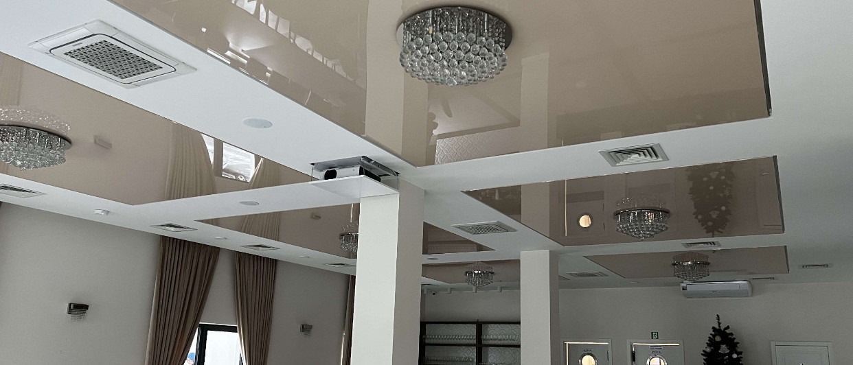 Beżowy, lustrzany sufit napinany z wbudowanym projektorem i klimatyzacją, oświetlony kryształowymi żyrandolami w przestronnym wnętrzu.