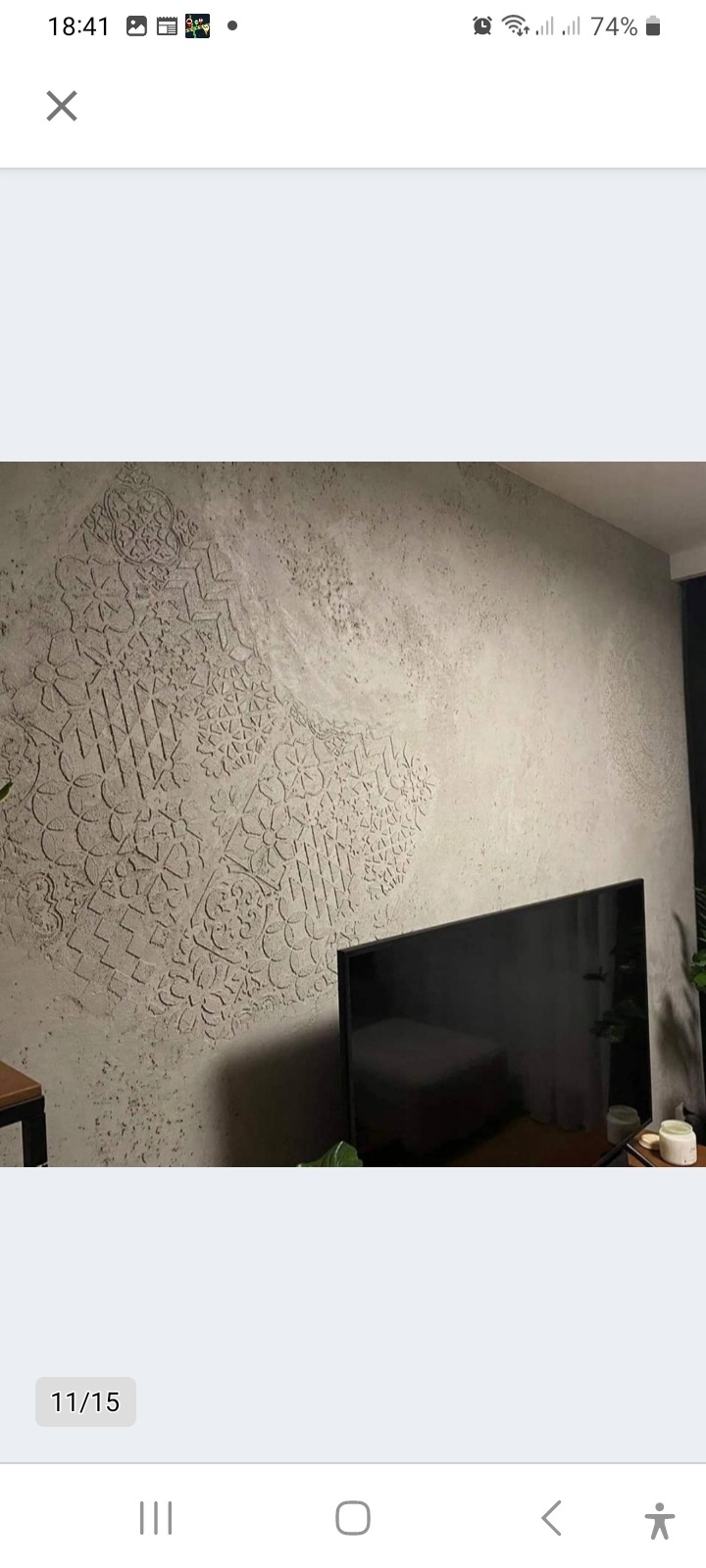 Dekoracyjna ściana w salonie z szarą fakturą i ornamentami geometrycznymi. Na pierwszym planie telewizor i roślina doniczkowa.