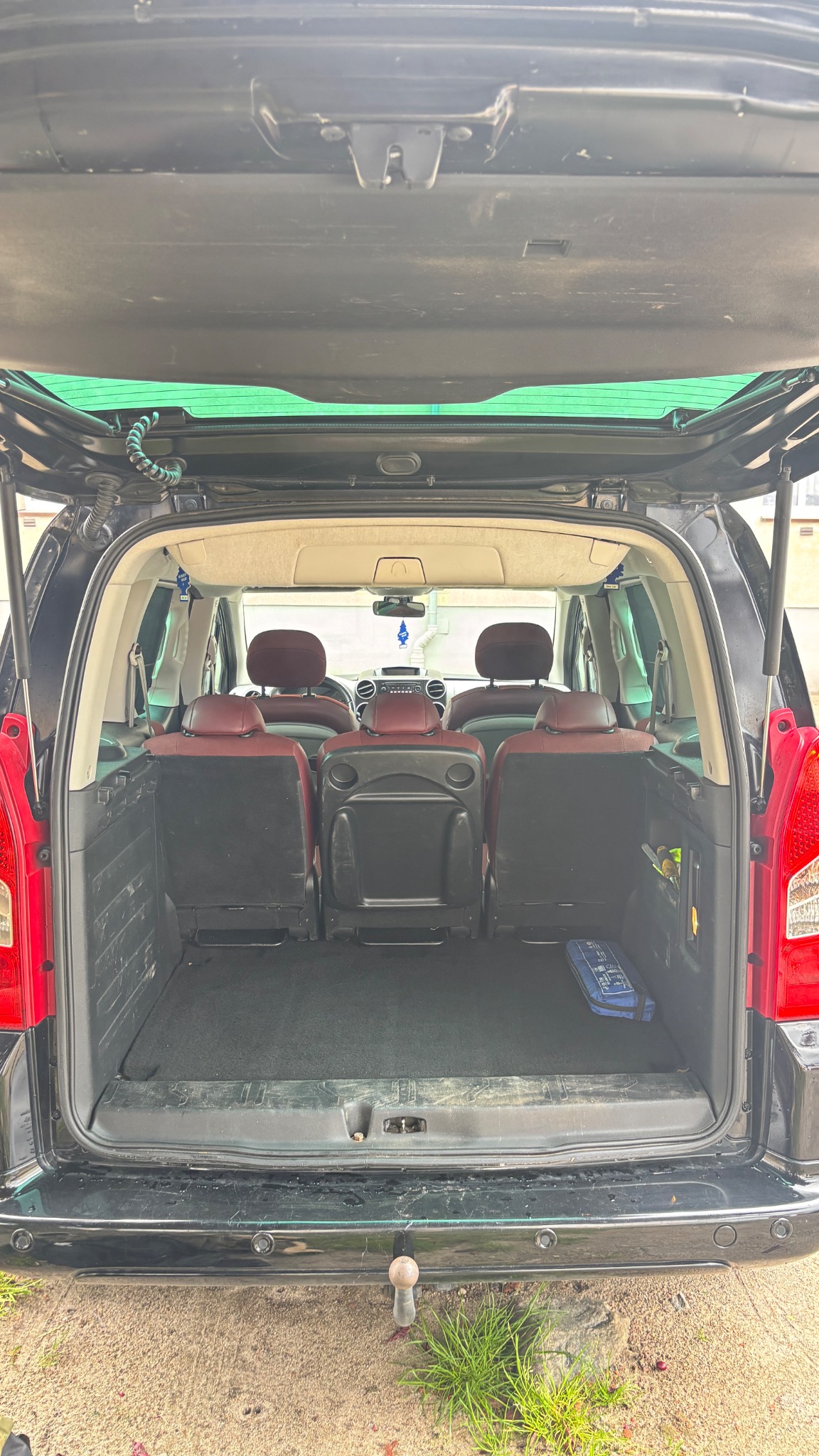 Otwarty bagażnik czarnego minivana z widocznymi trzema rzędami siedzeń, apteczką i hakiem holowniczym. Widok z tyłu pojazdu.