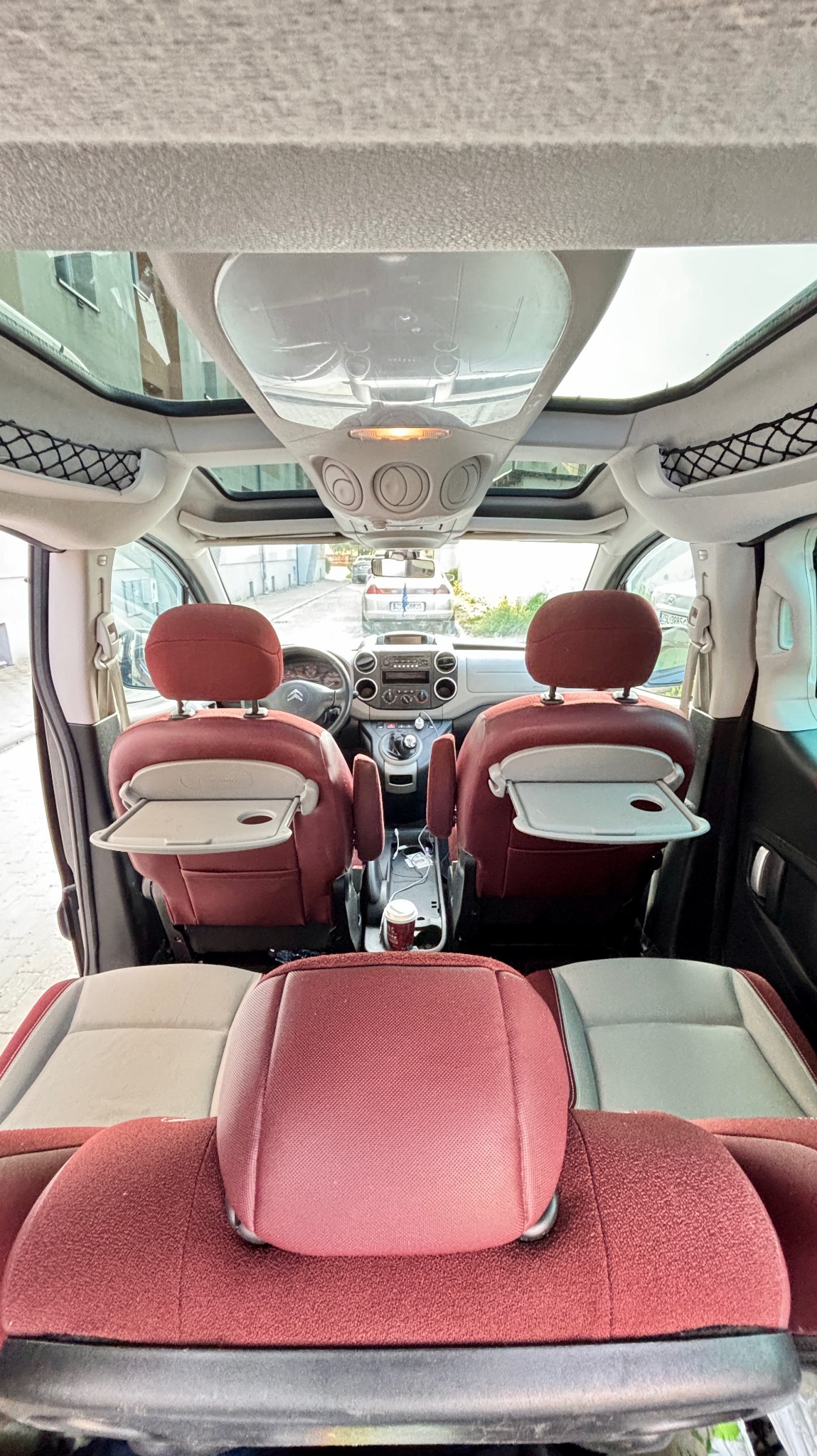 Wnętrze przestronnego vana z panoramicznym dachem. Widoczne siedzenia z rozkładanymi stolikami i elementami w kolorze burgundu, sugerujące komfortową podróż.