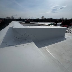 Roof-Bud - Biała, płaska powierzchnia dachu z obróbkami blacharskimi i narzędziami w tle, widziana z perspektywy dachu w słoneczny dzień.