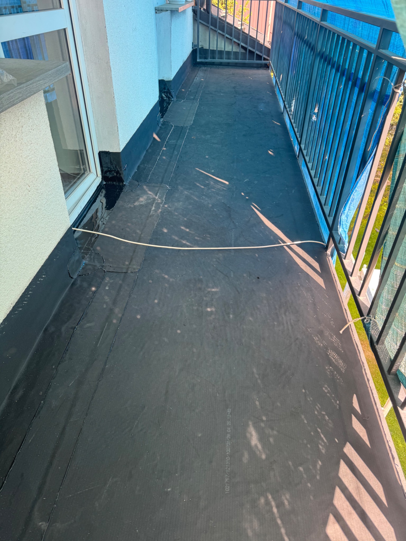 Wykończony balkon z czarną, bitumiczną izolacją, zabezpieczony balustradą. Widoczne detale łączeń i zabezpieczeń przy ścianie budynku.