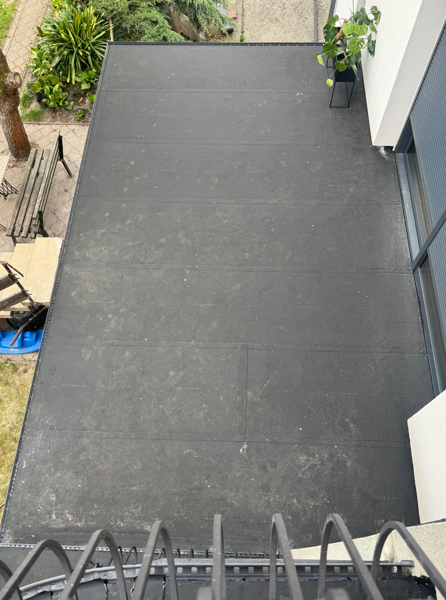 Czarny, płaski dach pokryty papą termozgrzewalną widziany z góry, z widocznymi śladami użytkowania i detalami wykończenia krawędzi.