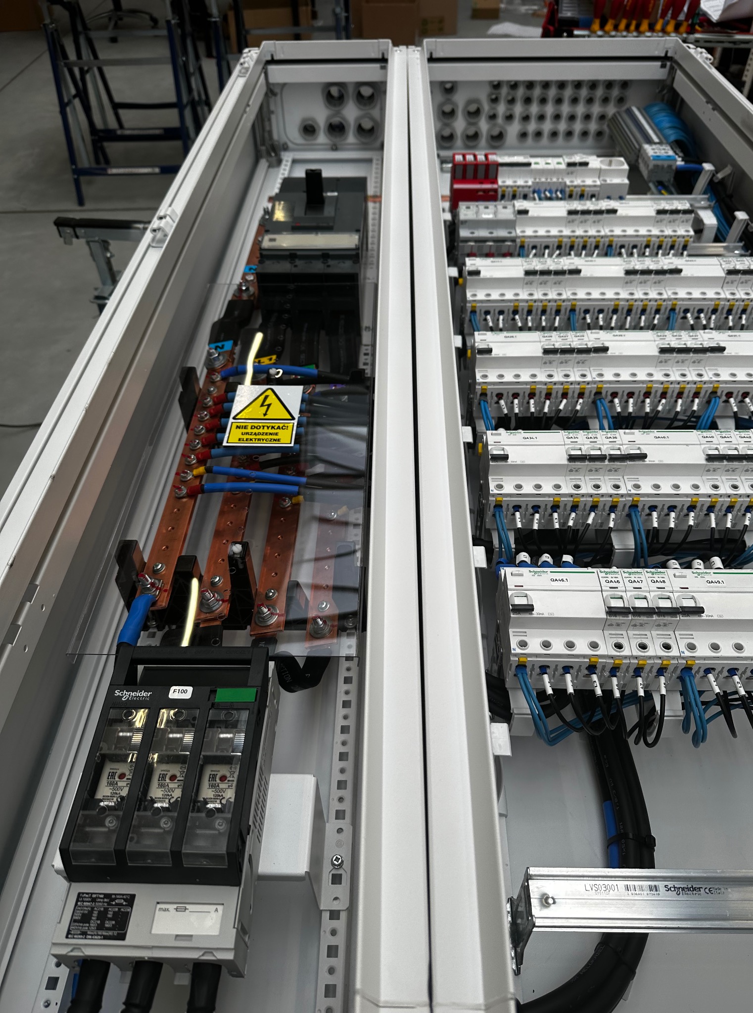 Rozdzielnica elektryczna z bezpiecznikami, okablowaniem i oznaczeniami ostrzegawczymi. Widoczne elementy marki Schneider Electric.