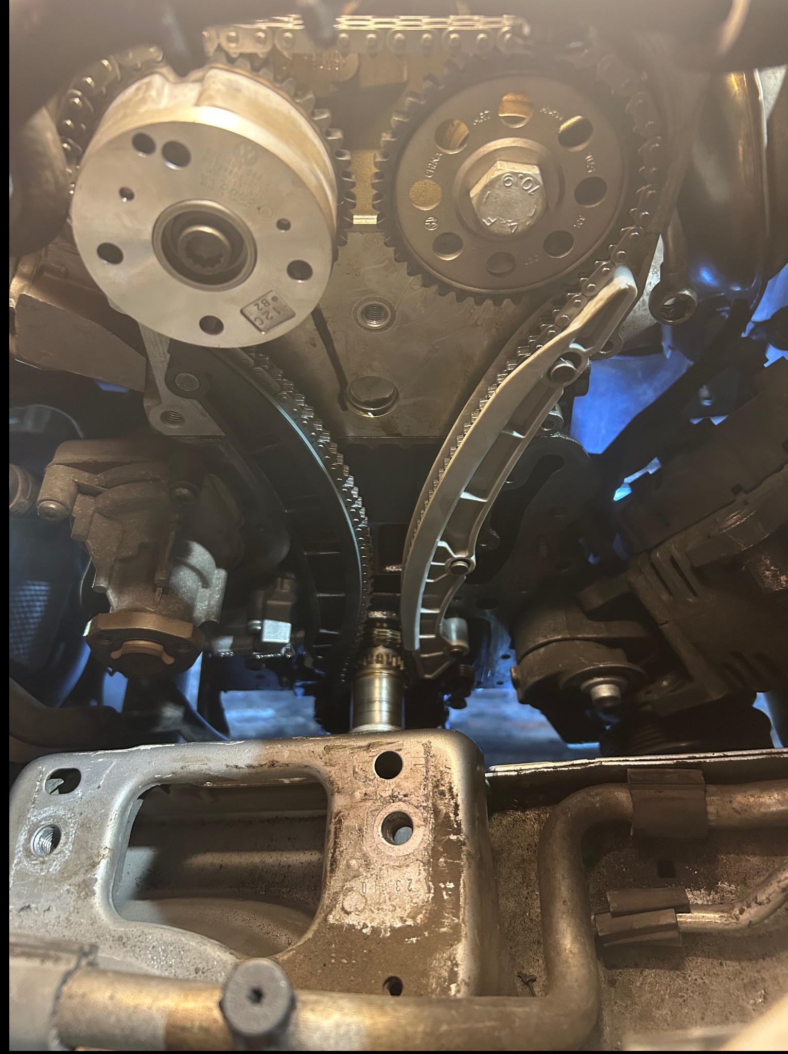 Otwarty silnik samochodowy z widocznym łańcuchem rozrządu, zębatkami i napinaczem w trakcie naprawy. Widoczne ślady oleju.