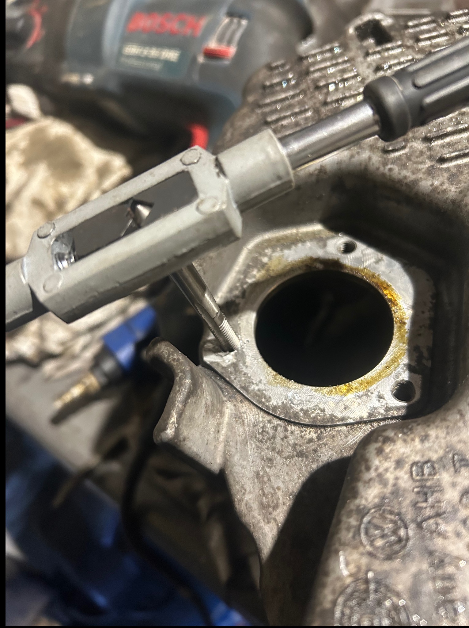 Gwintowanie otworu w metalowej części silnika samochodowego za pomocą gwintownika. Widoczne ślady oleju i zabrudzenia, sugerujące pracę warsztatową.