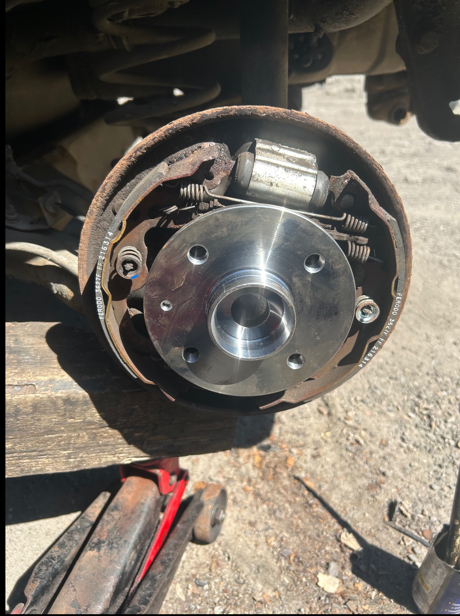 Wymienione szczęki hamulcowe w bębnie z widoczną piastą koła, sprężynami i cylindrem hamulcowym. Widoczny podnośnik i oznaczenia na szczękach.