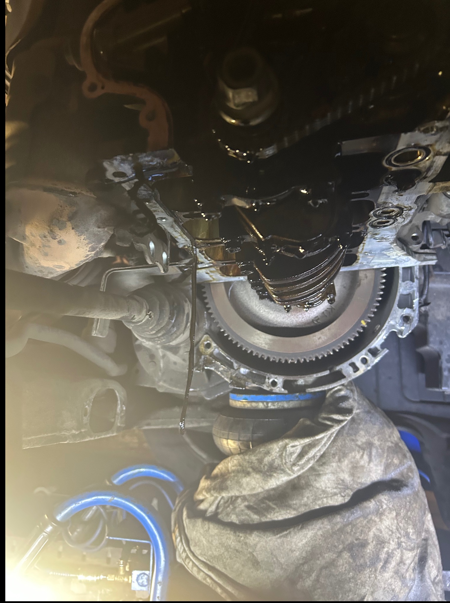 Silnik samochodowy w trakcie naprawy, widoczne elementy mechaniczne i wyciekający olej. Ujęcie z dołu, praca w warsztacie.