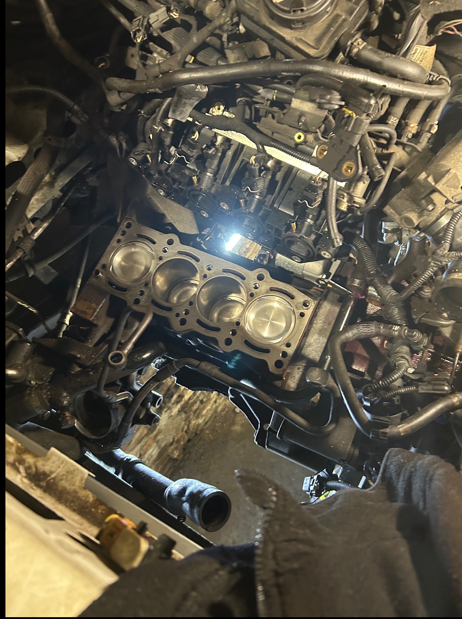 Otwarty silnik samochodowy z widocznymi cylindrami i tłokami, oświetlony punktowo, ukazujący etap prac naprawczych w warsztacie.