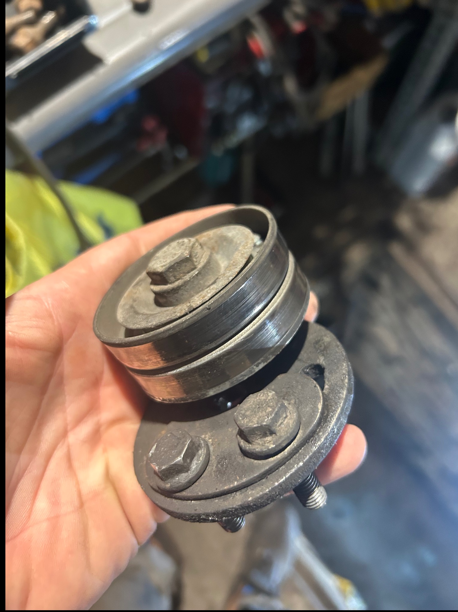 Zużyte koło pasowe w dłoni, widoczne ślady eksploatacji i rdzawy osad. Tło warsztatowe, narzędzia w tle. Bliski plan, ostre światło.