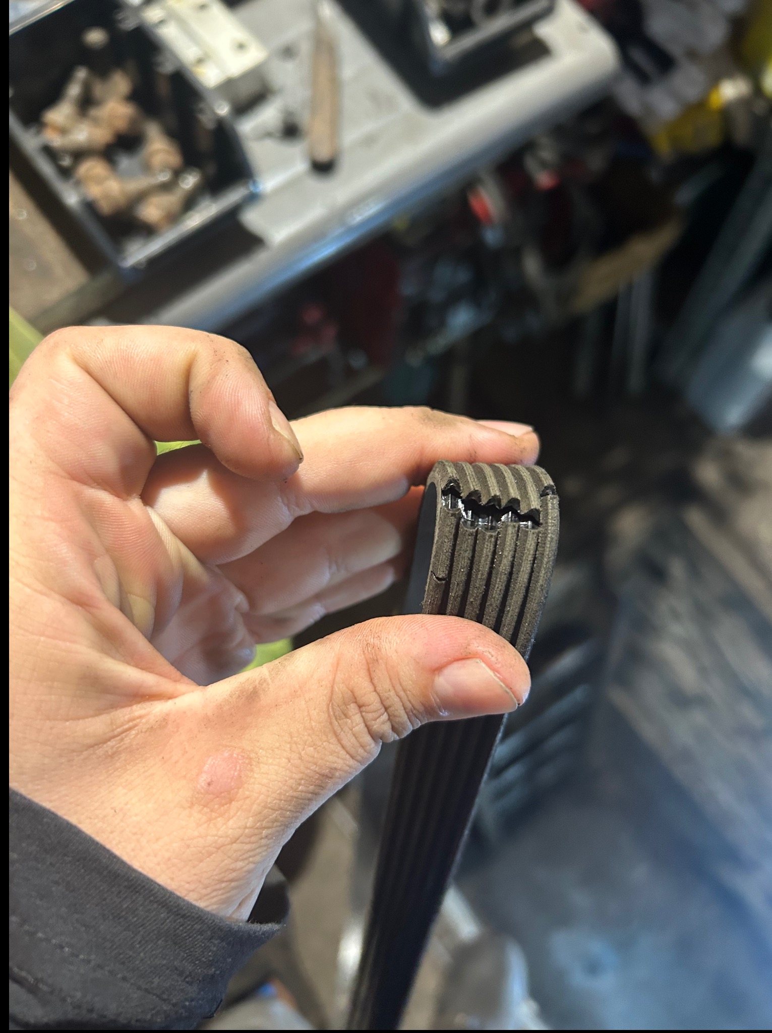 Zużyty pasek klinowy w dłoni mechanika, widoczne pęknięcia i uszkodzenia. Tło warsztatowe, narzędzia w tle. Detal zużycia.