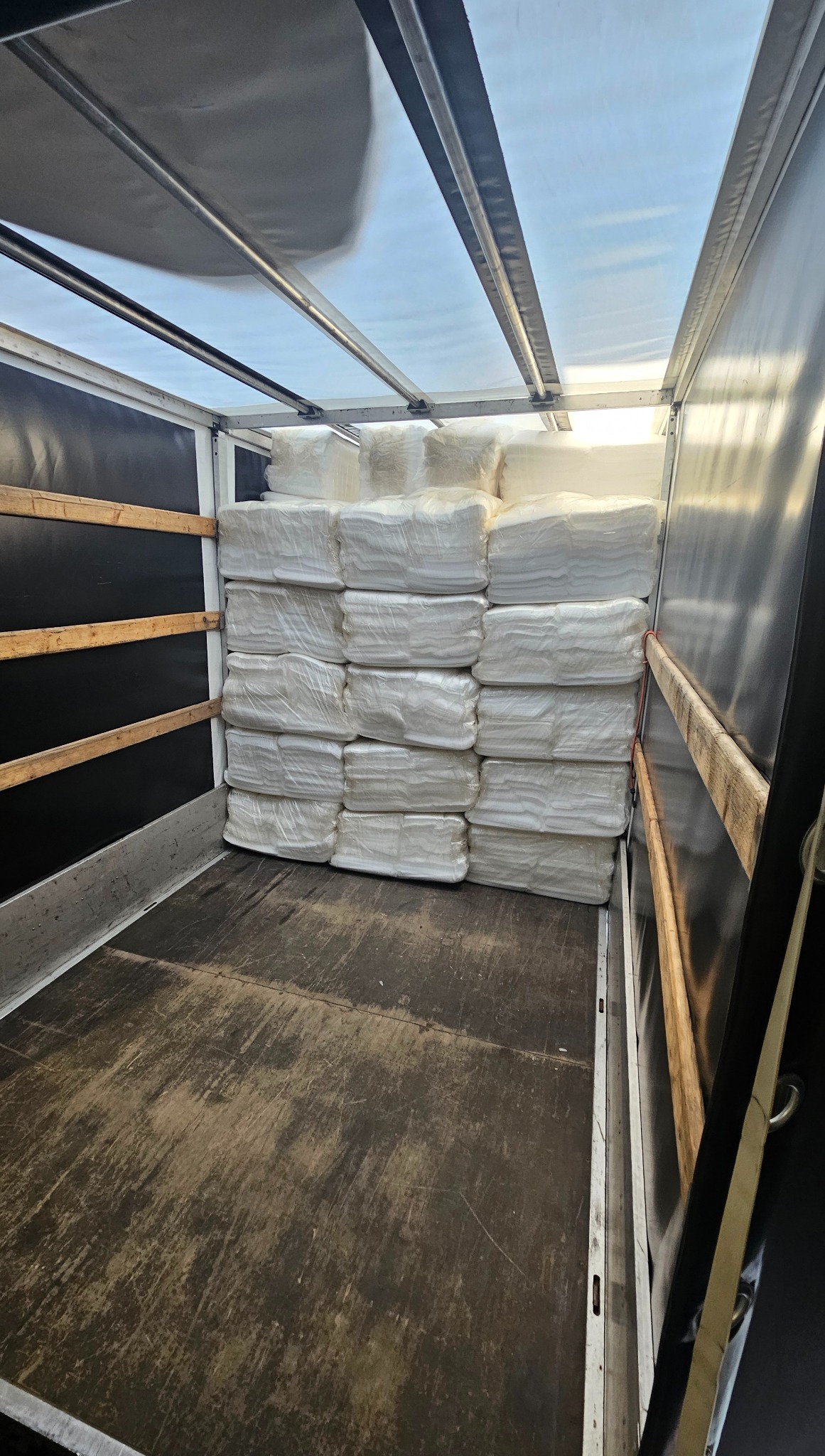 Wnętrze busa wypełnione białymi, zapakowanymi paczkami. Widoczna podłoga i ściany przestrzeni ładunkowej. Ujęcie z głębi pojazdu.