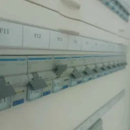 Rozdzielnica elektryczna Hager z bezpiecznikami, widok z boku, etykiety F11-F15, niektóre wyłączniki w pozycji wyłączonej.