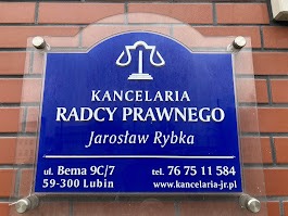 Szyld informacyjny kancelarii radcy prawnego Jarosława Rybki z adresem i numerem telefonu, umieszczony na ceglanej ścianie budynku w Lubinie.