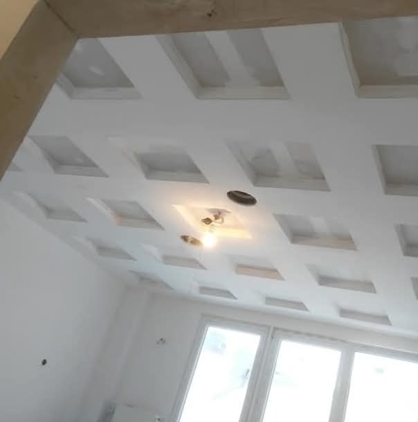Biały sufit podwieszany z kwadratowymi wgłębieniami i oświetleniem w nowo wyremontowanym pokoju z oknami, widok z dołu.