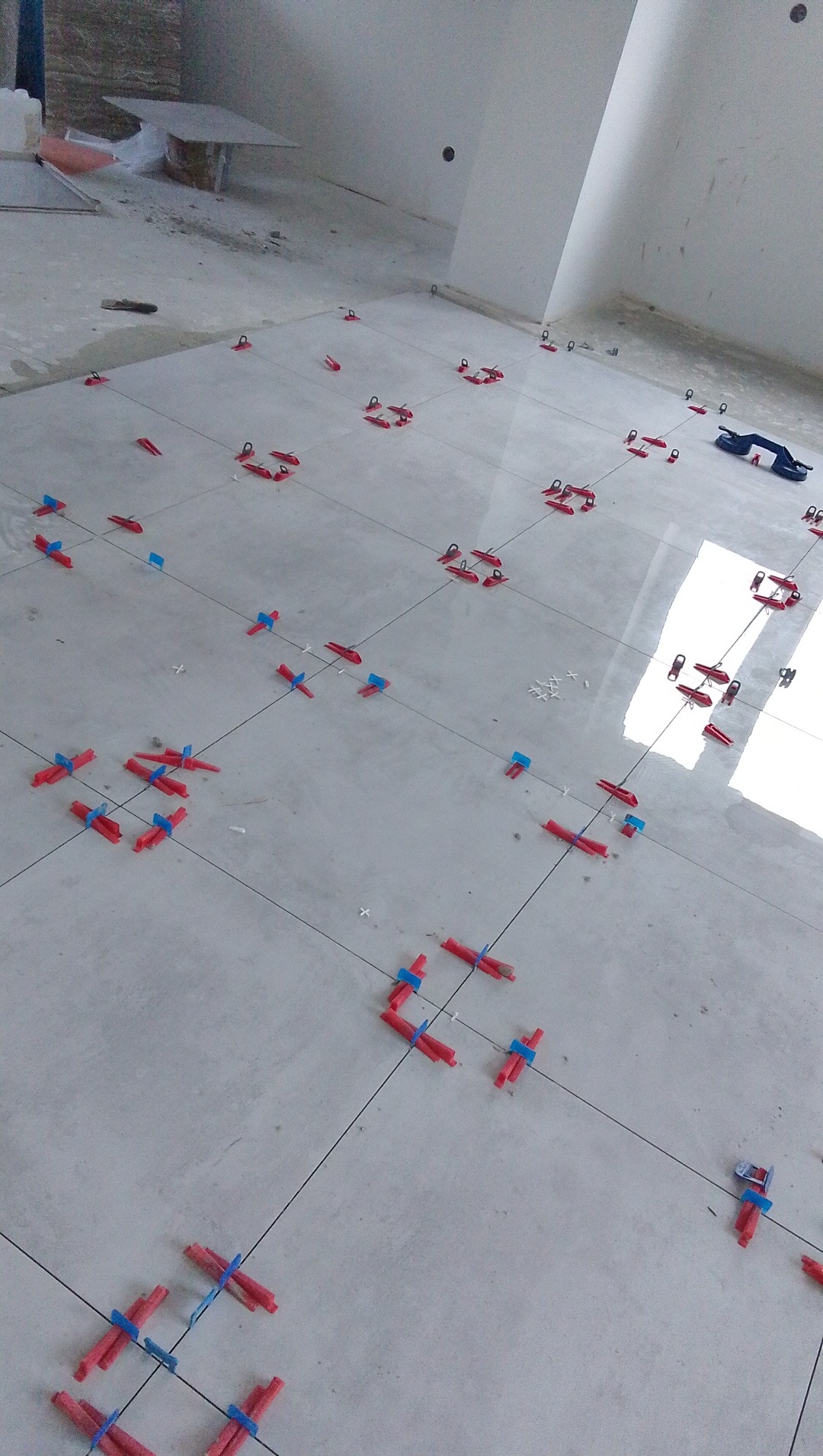 Układanie płytek podłogowych z użyciem klipsów poziomujących. Widoczne świeżo ułożone płytki i narzędzia glazurnicze. Jasne wnętrze w trakcie prac wykończeniowych.