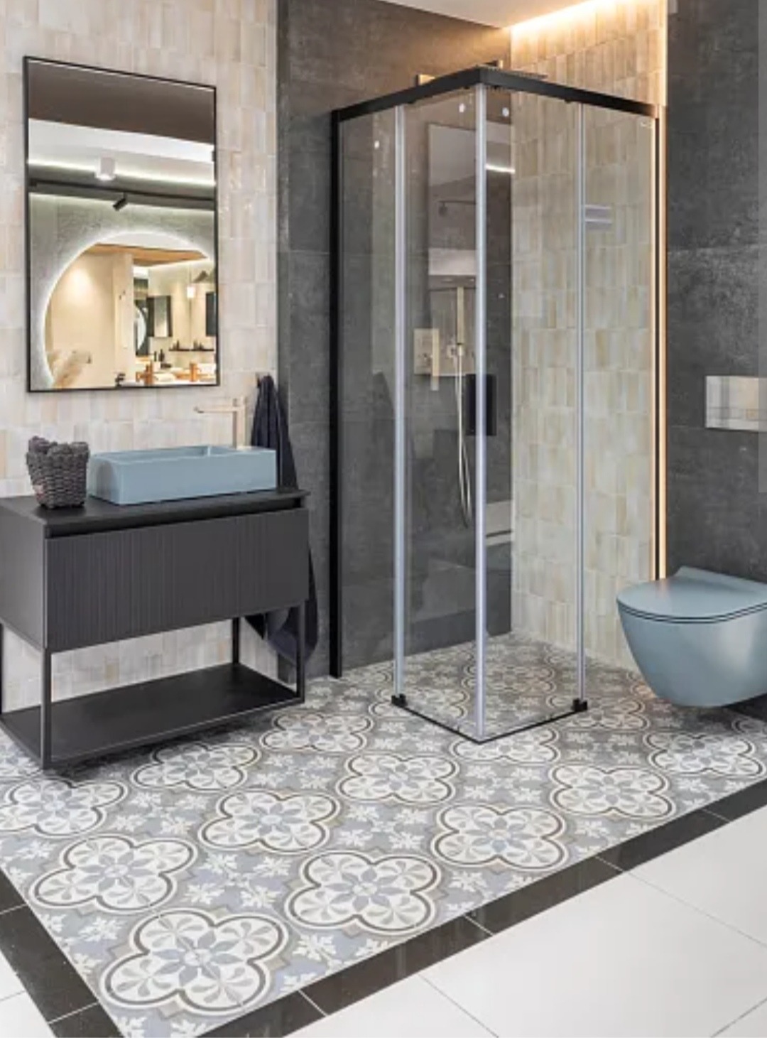 Nowoczesna łazienka z kabiną prysznicową, umywalką na szafce i toaletą w odcieniach szarości i beżu. Wzorzysta podłoga i lustro z podświetleniem LED.