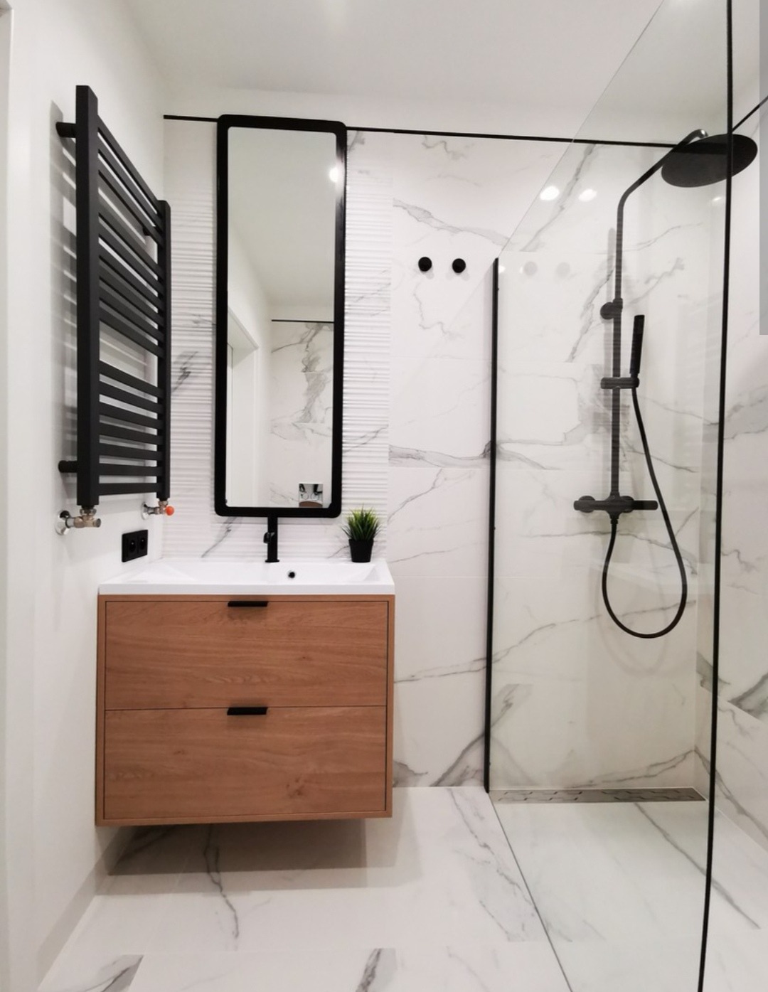 Nowoczesna łazienka z drewnianą szafką pod umywalką, czarnym grzejnikiem drabinkowym i kabiną prysznicową typu walk-in z armaturą w czarnym macie.