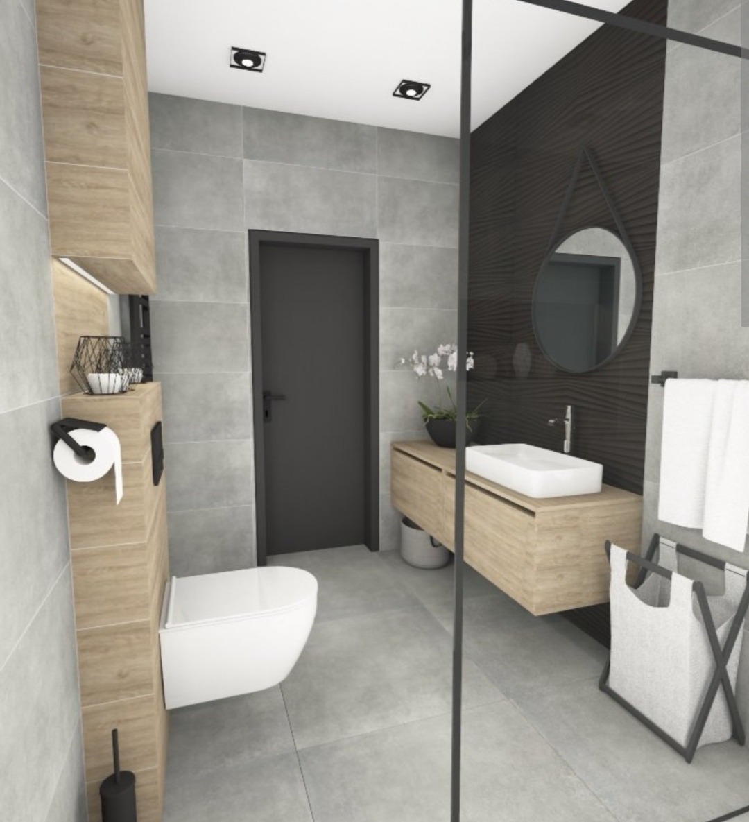 Nowoczesna łazienka z szarymi płytkami, drewnianymi akcentami i minimalistyczną armaturą. Wisząca toaleta, umywalka na szafce i okrągłe lustro.