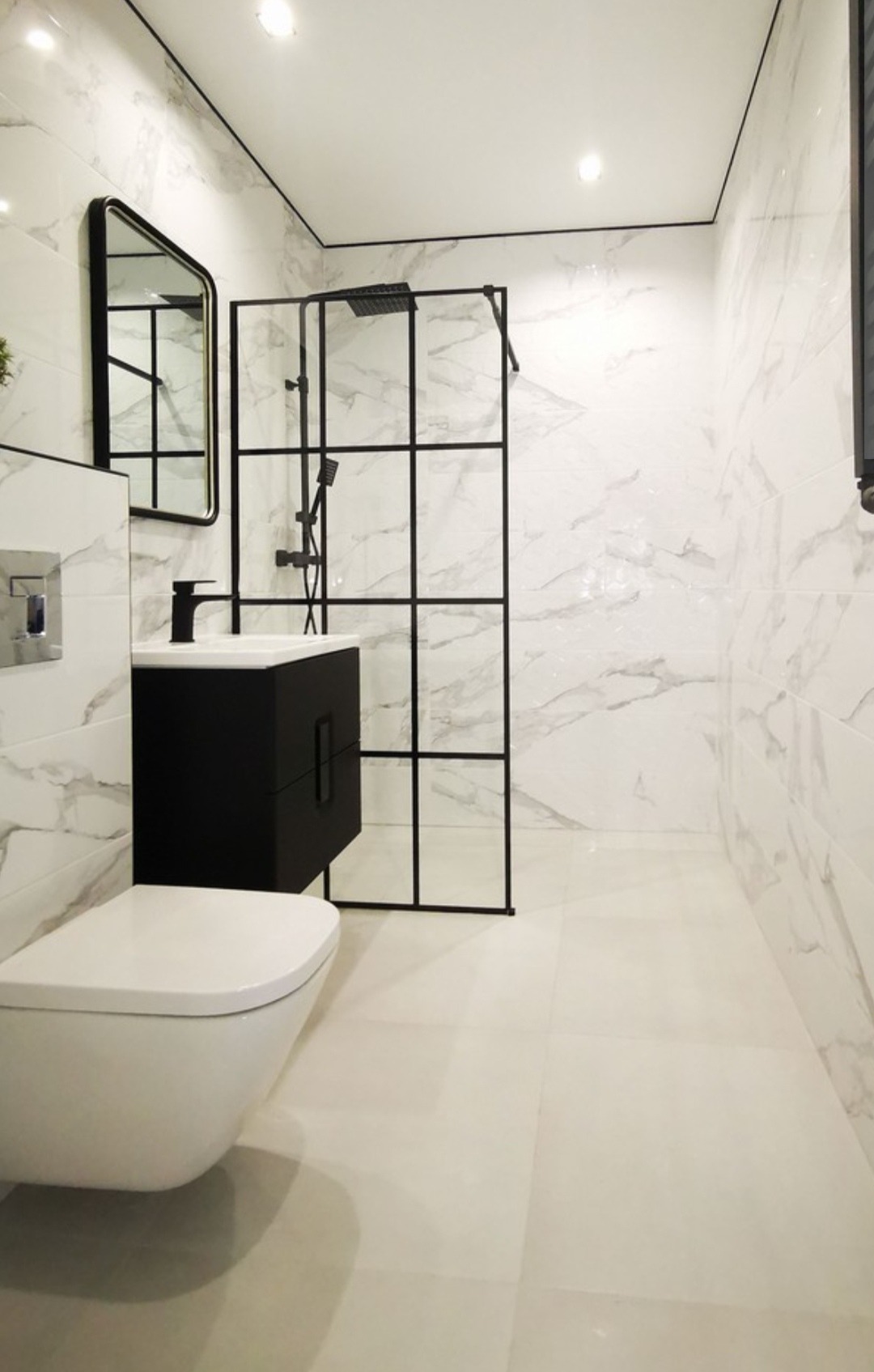 Nowoczesna łazienka z kabiną prysznicową typu walk-in, czarną armaturą i białymi płytkami imitującymi marmur. Minimalistyczny design z wiszącą szafką umywalkową.