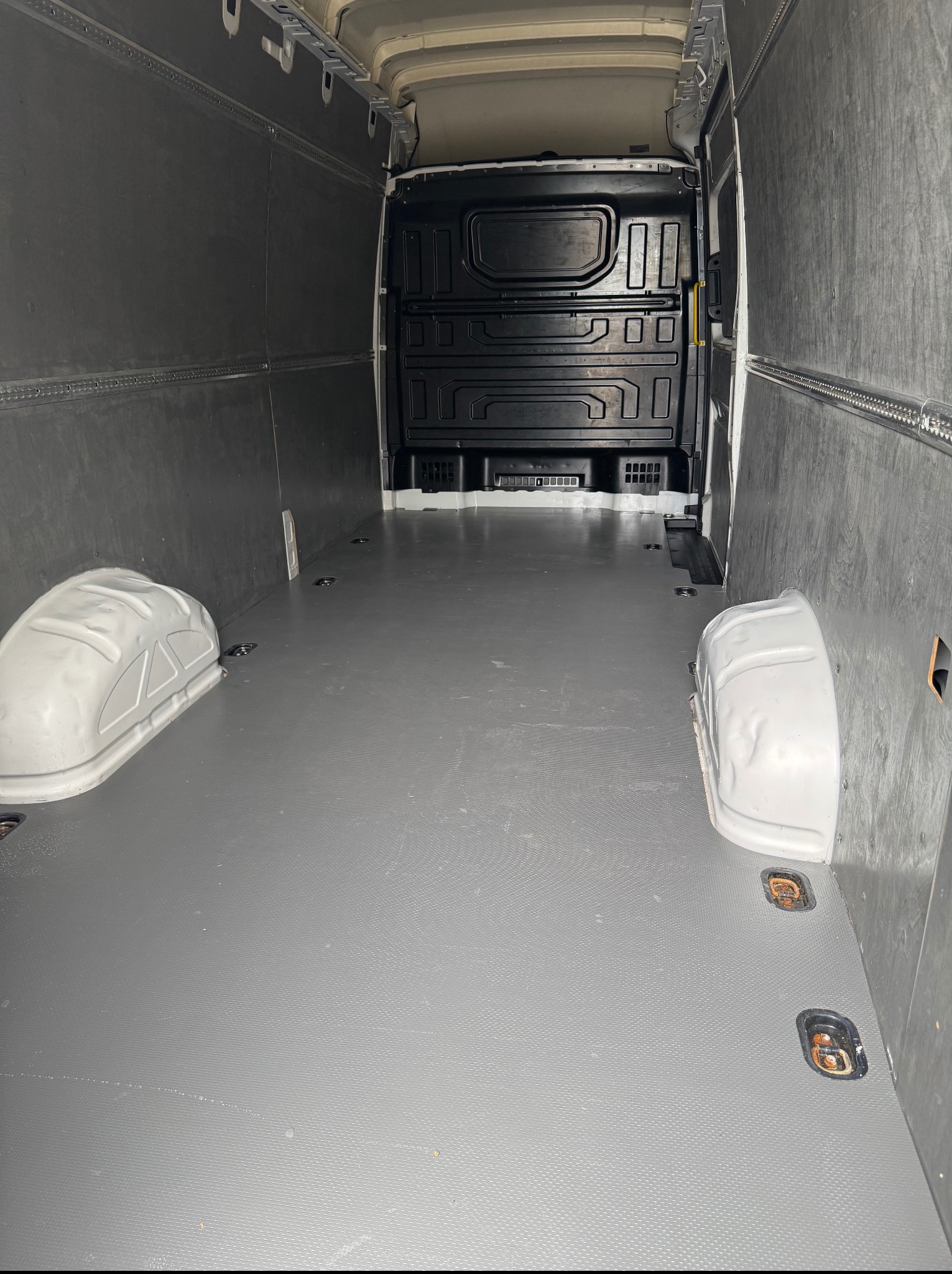 Wnętrze pustego, wyłożonego szarą podłogą i ciemnymi panelami busa. Widoczne uchwyty mocujące w podłodze i osłony nadkoli. Perspektywa z tylnych drzwi.