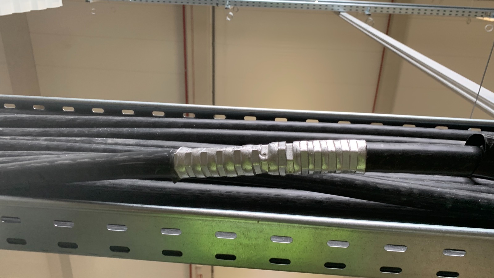 Zamocowany pęk czarnych kabli elektrycznych w metalowej korycie kablowej, zabezpieczony srebrną taśmą izolacyjną w hali przemysłowej.