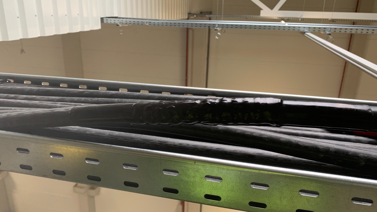 Zamknięty korytkowy system kablowy z czarnymi kablami w hali przemysłowej. Widoczne łączenie kabli zabezpieczone taśmą izolacyjną.